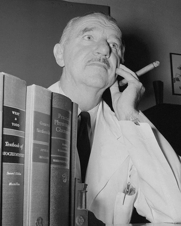 Vincent du Vigneaud sentado junto a una estantería de libros, con un puro